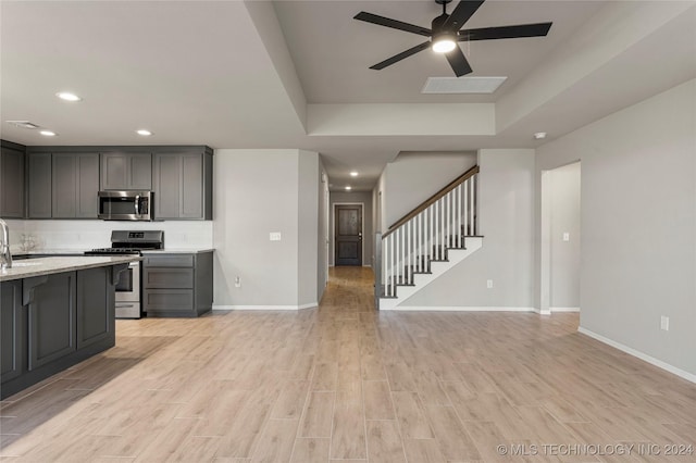 kitchen featuring gray cabinetry, stainless steel appliances, a raised ceiling, ceiling fan, and light hardwood / wood-style floors