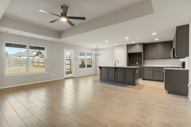 kitchen with ceiling fan with notable chandelier, a kitchen island with sink, hanging light fixtures, and light hardwood / wood-style flooring