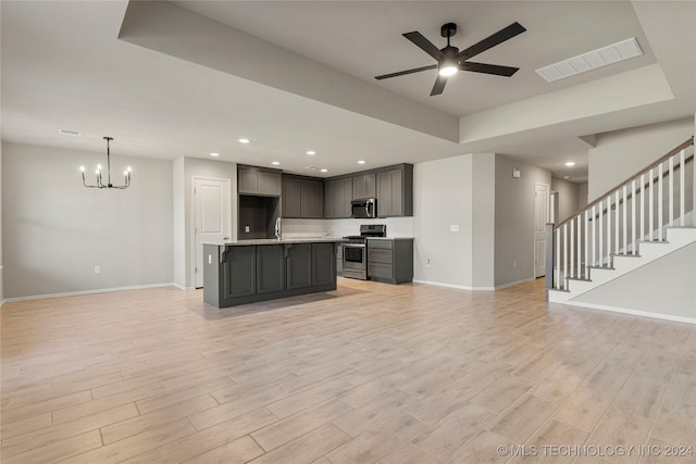 kitchen with appliances with stainless steel finishes, ceiling fan with notable chandelier, light hardwood / wood-style floors, and a kitchen island with sink