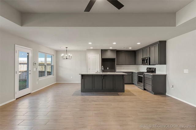 kitchen with appliances with stainless steel finishes, ceiling fan with notable chandelier, a kitchen island with sink, sink, and hanging light fixtures