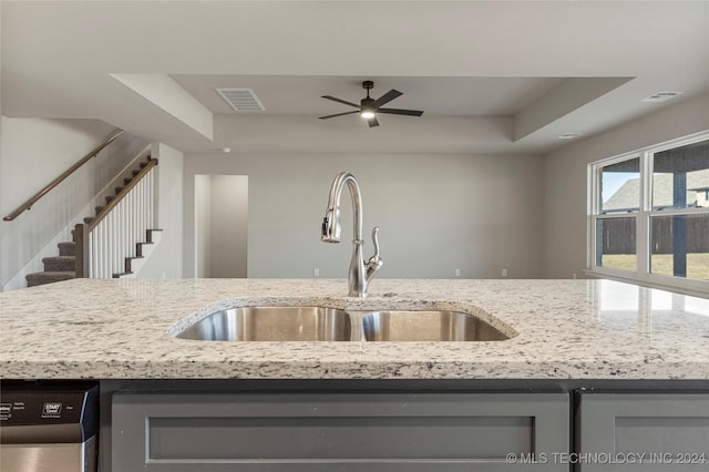 kitchen with dishwasher, a raised ceiling, light stone countertops, and sink