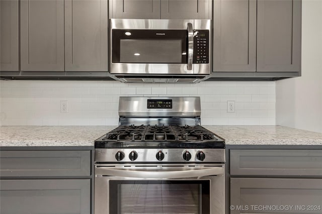 kitchen featuring light stone countertops, appliances with stainless steel finishes, gray cabinets, and decorative backsplash