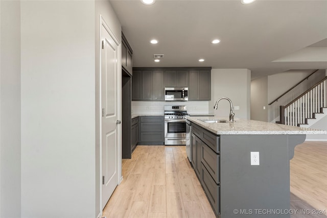 kitchen featuring gray cabinetry, a center island with sink, sink, light hardwood / wood-style flooring, and appliances with stainless steel finishes