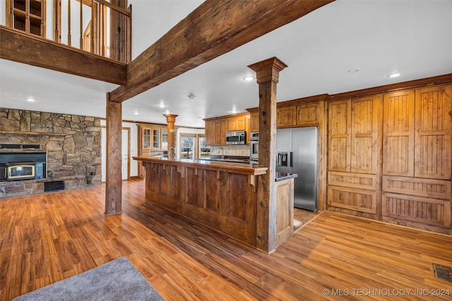 kitchen featuring kitchen peninsula, appliances with stainless steel finishes, a kitchen breakfast bar, light hardwood / wood-style floors, and a wood stove