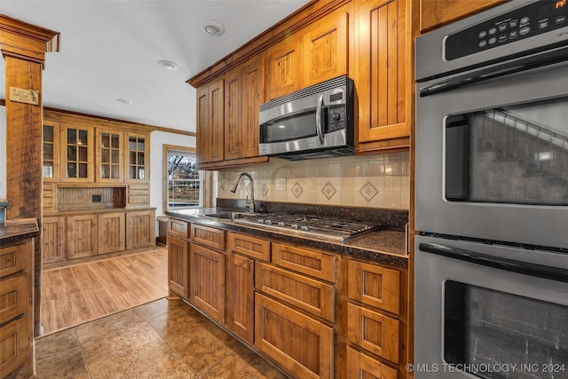 kitchen featuring appliances with stainless steel finishes, tasteful backsplash, ornamental molding, dark stone counters, and hardwood / wood-style flooring