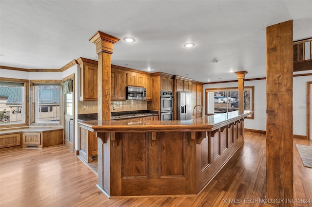 kitchen featuring stainless steel appliances, tasteful backsplash, light hardwood / wood-style flooring, decorative columns, and a breakfast bar