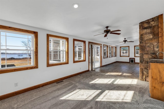 unfurnished living room featuring dark carpet, ceiling fan, and sink