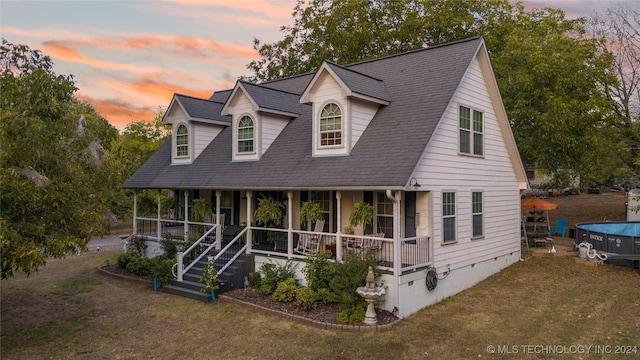 cape cod house with a yard and covered porch