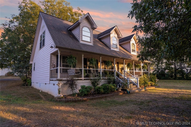 new england style home featuring covered porch and a yard