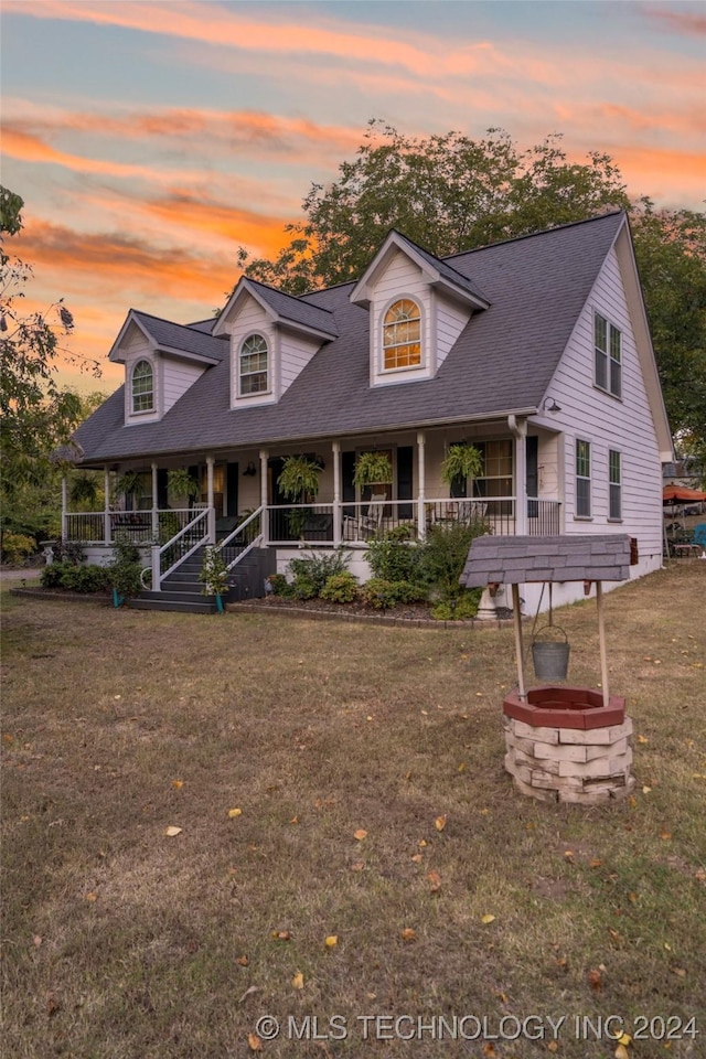 cape cod home with covered porch, an outdoor fire pit, and a lawn