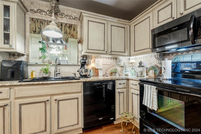 kitchen featuring black appliances, hanging light fixtures, sink, cream cabinetry, and light hardwood / wood-style floors