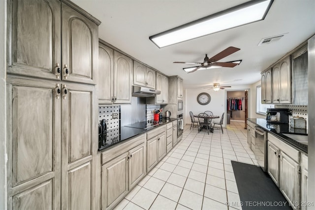 kitchen featuring dark countertops, under cabinet range hood, light tile patterned floors, and stainless steel appliances