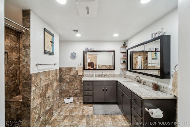 full bathroom with tile walls, visible vents, a sink, and tiled shower