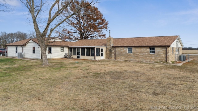 rear view of property featuring central air condition unit, a sunroom, stone siding, a lawn, and a chimney