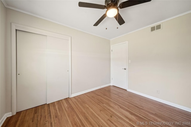 unfurnished bedroom with wood-type flooring, a closet, ceiling fan, and crown molding