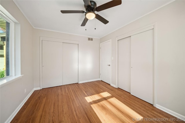 unfurnished bedroom with hardwood / wood-style floors, ceiling fan, crown molding, and two closets