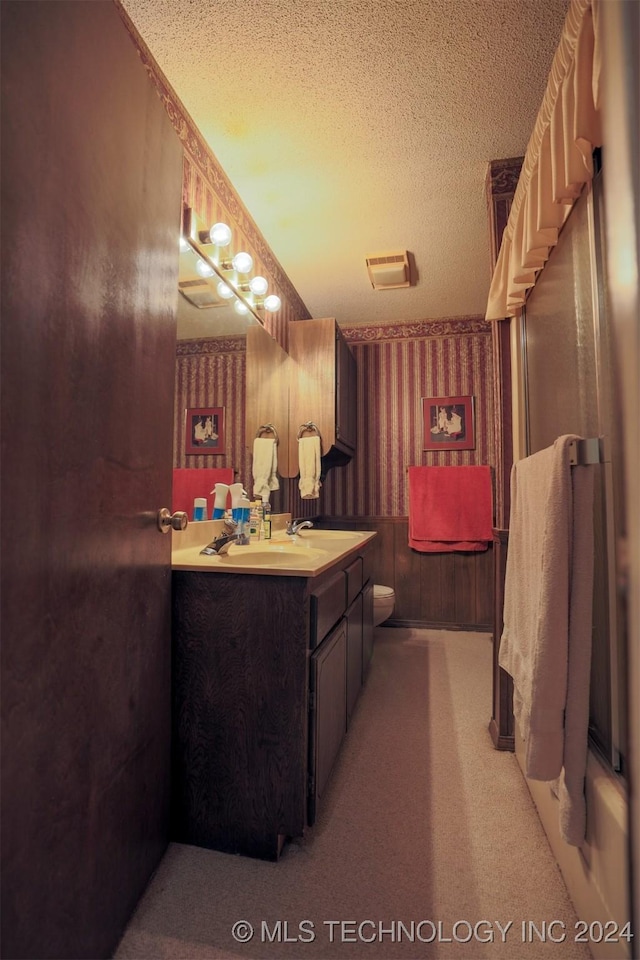 bathroom featuring vanity, a textured ceiling, toilet, and wooden walls