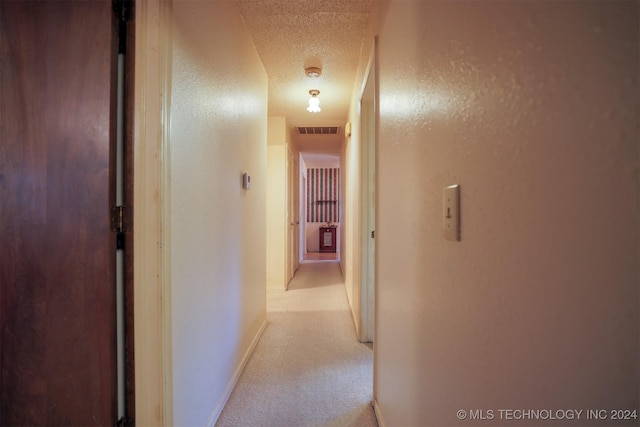 corridor featuring a textured ceiling and light colored carpet