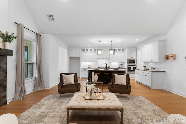 living room featuring sink, light hardwood / wood-style floors, vaulted ceiling, and a brick fireplace