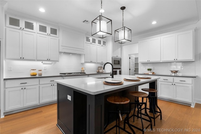 kitchen featuring white cabinets, light wood-type flooring, and an island with sink