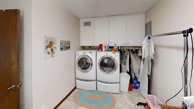 clothes washing area with washing machine and dryer, cabinets, and light tile patterned flooring