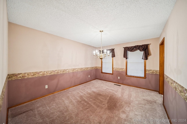 carpeted empty room featuring a textured ceiling and a chandelier