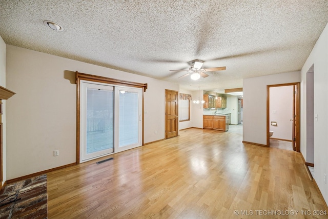 unfurnished living room with ceiling fan with notable chandelier, light wood-type flooring, and a textured ceiling