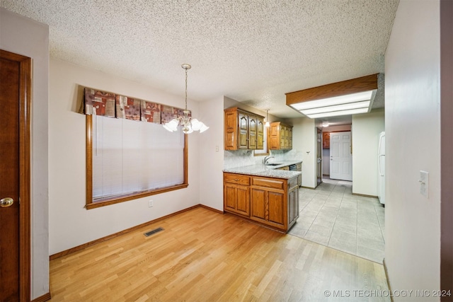 kitchen featuring backsplash, a textured ceiling, pendant lighting, a notable chandelier, and light hardwood / wood-style floors