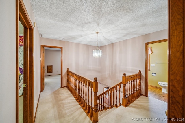 corridor with a notable chandelier, light colored carpet, and a textured ceiling