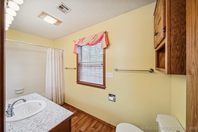 bathroom featuring walk in shower, vanity, a textured ceiling, hardwood / wood-style flooring, and toilet