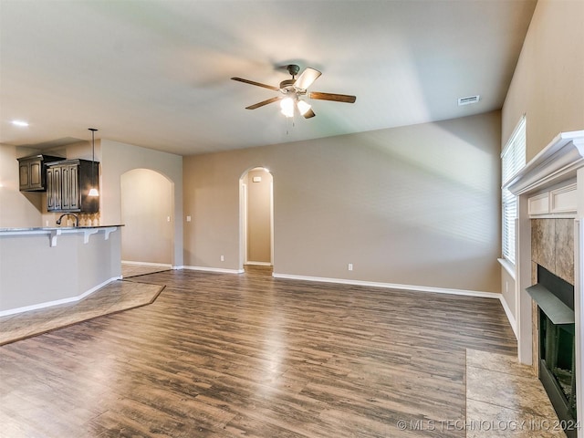 unfurnished living room featuring a tiled fireplace, ceiling fan, and dark wood-type flooring