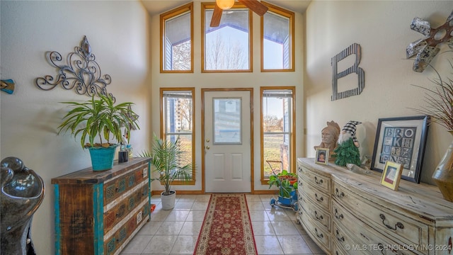 entrance foyer featuring ceiling fan, a healthy amount of sunlight, light tile patterned flooring, and a towering ceiling