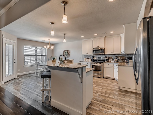 kitchen featuring hanging light fixtures, a breakfast bar area, a center island with sink, white cabinets, and appliances with stainless steel finishes