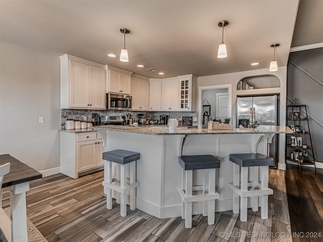 kitchen with pendant lighting, white cabinetry, stainless steel appliances, and an island with sink