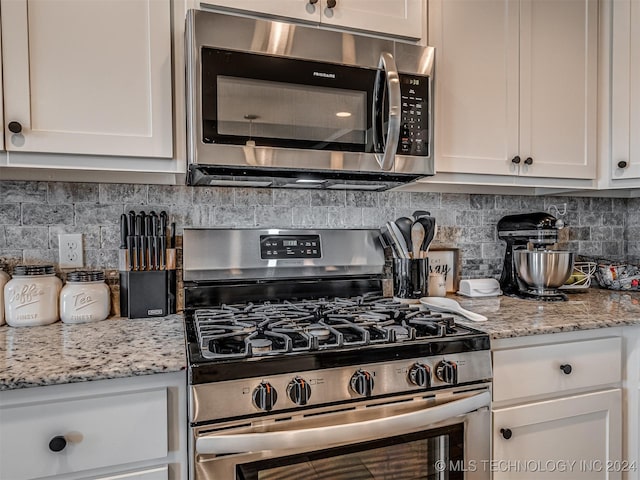 kitchen with light stone countertops, decorative backsplash, white cabinets, and stainless steel appliances