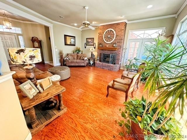 living room with hardwood / wood-style flooring, ceiling fan, ornamental molding, and a fireplace