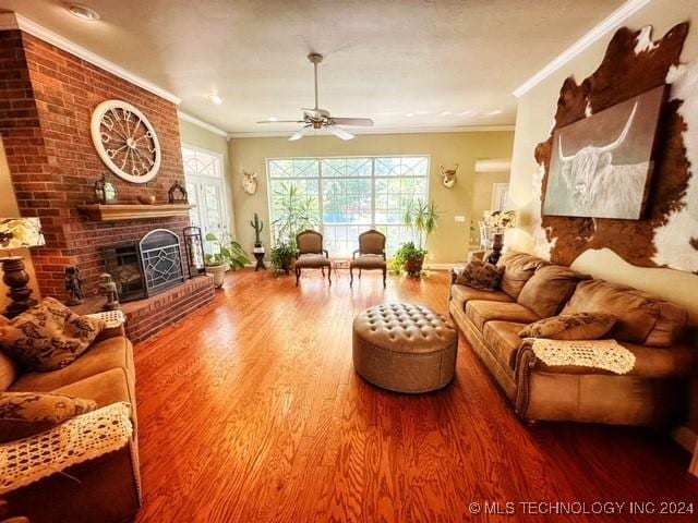 living room with hardwood / wood-style flooring, ceiling fan, ornamental molding, and a fireplace