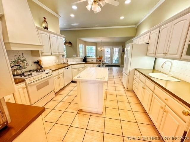 kitchen with custom exhaust hood, white appliances, sink, light tile patterned flooring, and kitchen peninsula