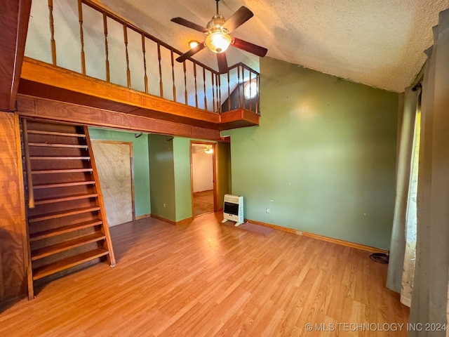 unfurnished living room with a textured ceiling, heating unit, ceiling fan, high vaulted ceiling, and light hardwood / wood-style flooring