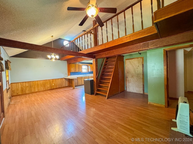 unfurnished living room with wood walls, ceiling fan with notable chandelier, hardwood / wood-style flooring, a textured ceiling, and heating unit