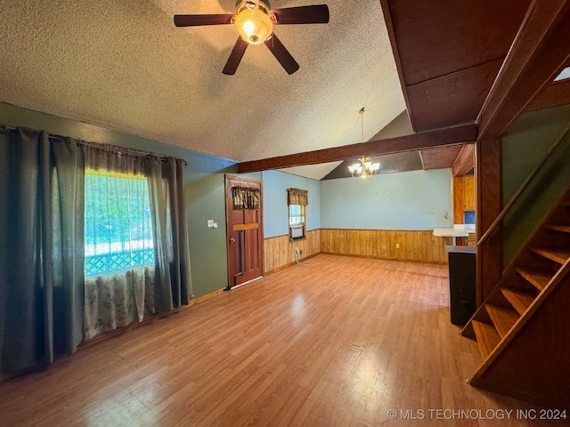 unfurnished living room featuring wood walls, ceiling fan with notable chandelier, vaulted ceiling, hardwood / wood-style flooring, and a textured ceiling