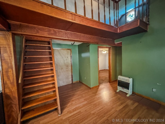 staircase with heating unit, ceiling fan, and wood-type flooring