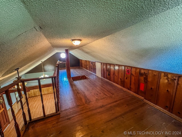 bonus room with vaulted ceiling, wooden walls, a textured ceiling, and hardwood / wood-style flooring