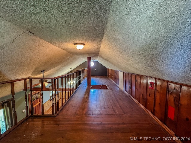 additional living space featuring dark hardwood / wood-style flooring, a textured ceiling, lofted ceiling, and wood walls