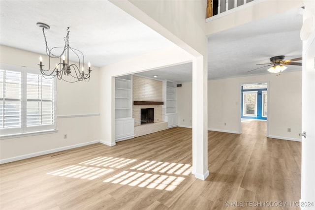 unfurnished living room featuring hardwood / wood-style flooring, ceiling fan with notable chandelier, a fireplace, and built in shelves