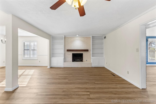 unfurnished living room with hardwood / wood-style flooring, a healthy amount of sunlight, a textured ceiling, and a brick fireplace