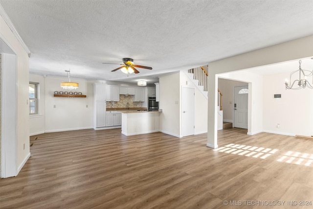 unfurnished living room featuring hardwood / wood-style flooring, ceiling fan with notable chandelier, sink, and a textured ceiling