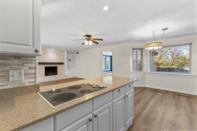 kitchen featuring pendant lighting, electric cooktop, light hardwood / wood-style flooring, a brick fireplace, and white cabinetry