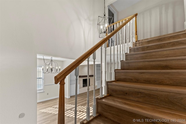 stairs with a chandelier, wood-type flooring, and a brick fireplace