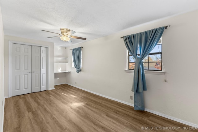 unfurnished bedroom featuring ceiling fan, wood-type flooring, a textured ceiling, and a closet